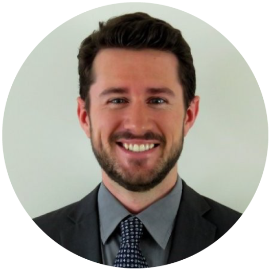 A younger white man with short, brown hair and a short beard wearing business attire