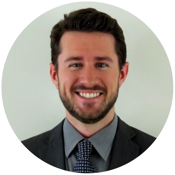 A younger white man with short, brown hair and a short beard wearing business attire
