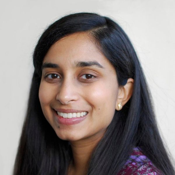 A younger woman of East Asian descent with long black hair smiling into the camera wearing a purple patterned top