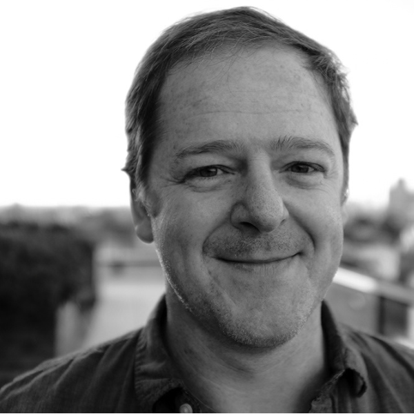 Black-and-white head shot of a middle-aged man with short hair and facial scruff, smiling